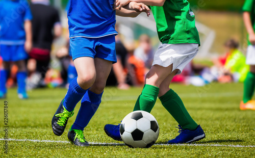 Fototapeta Naklejka Na Ścianę i Meble -  Boys kicking football match on the sports field. Kids soccer teams compete in the school soccer tournament. Children in blue and green sport jersey and football cleats.