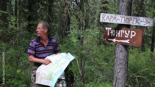 Tourist with a map near the signs. Inscriptions Tungur village, Kara Turek mountain. A man traveler got lost in a hike and is looking for a way on the map. photo