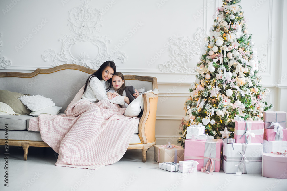 Two happy girls, mother and daughter siting on a sofa in Christmas decorated room. Two happy girls, mother and daughter siting on a sofa in Christmas decorated room.