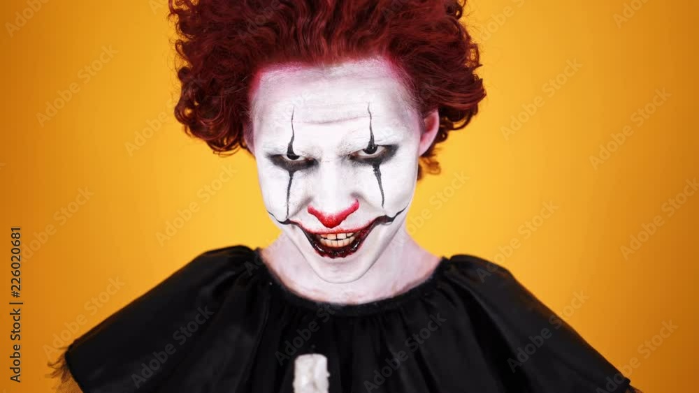 Close up view of Angry clown with halloween makeup holding candle and looking at the camera over orange background Close up view of Angry clown with halloween makeup holding candle and looking at the camera over orange background