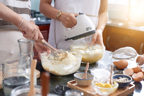 Bilde på lerret Unrecognizable women making cookie dough in kitchen, using whisk and modern elec