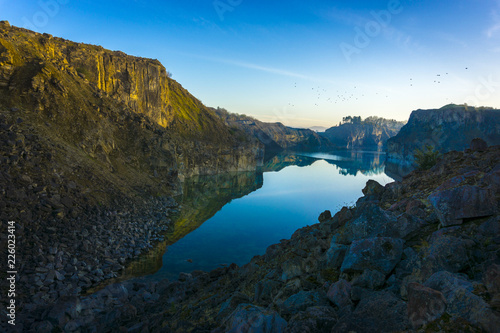 Summertime, abandoned quarry, sunrise, with clear blue sky, cool reflections of the surrounding rock faces on the surface of the lake.