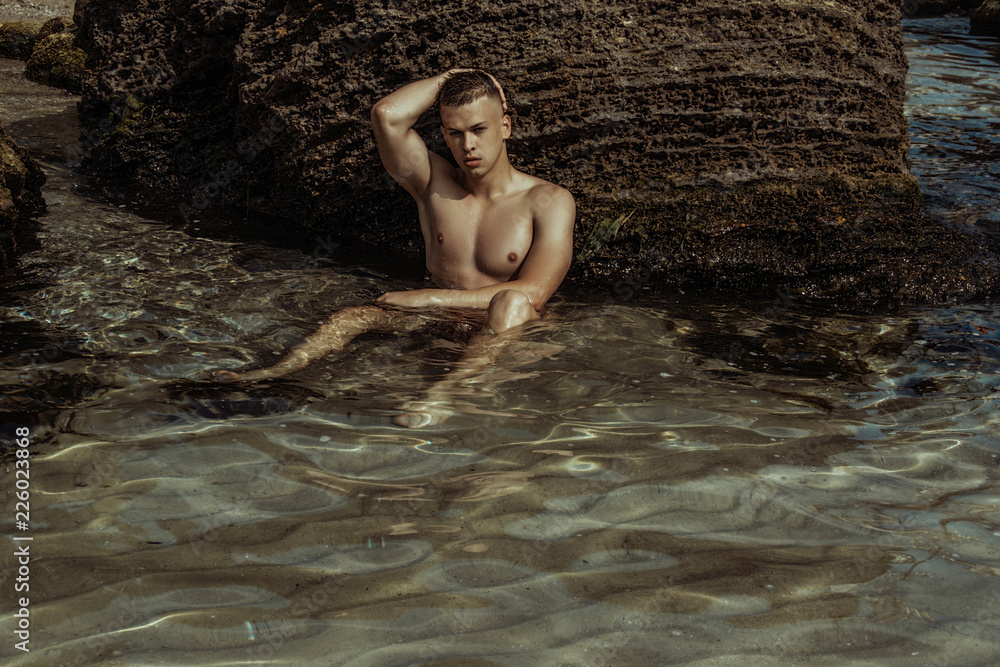 Fototapeta premium Strong face muscle male model on the nature background with sand stones and water on the beach on the sunset