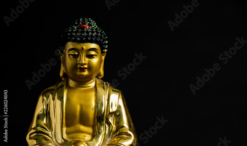 close up of Meditating Golden Buddha statue on black background