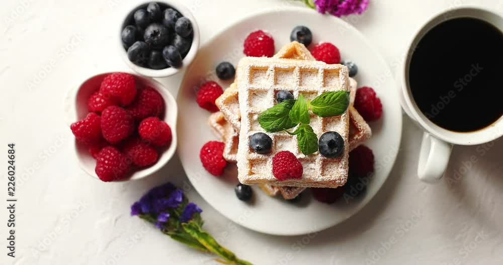 From above shot of cup of aromatic coffee and bowls with fresh berries standing near plate with delicious soft waffles From above shot of cup of aromatic coffee and bowls with fresh berries standing near plate with delicious soft waffles