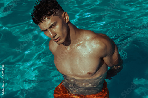 Strong face muscle male model in the open  summer shower on the vacation pool background with blue water on the nature beach on the sunset
