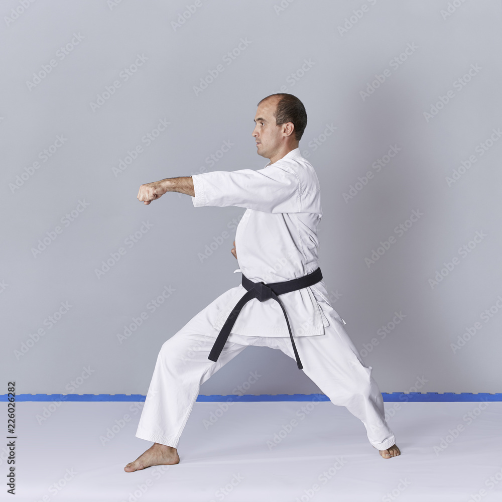 On a gray background, a young active athlete does formal karate exercises. On a gray background, a young active athlete does formal karate exercises.