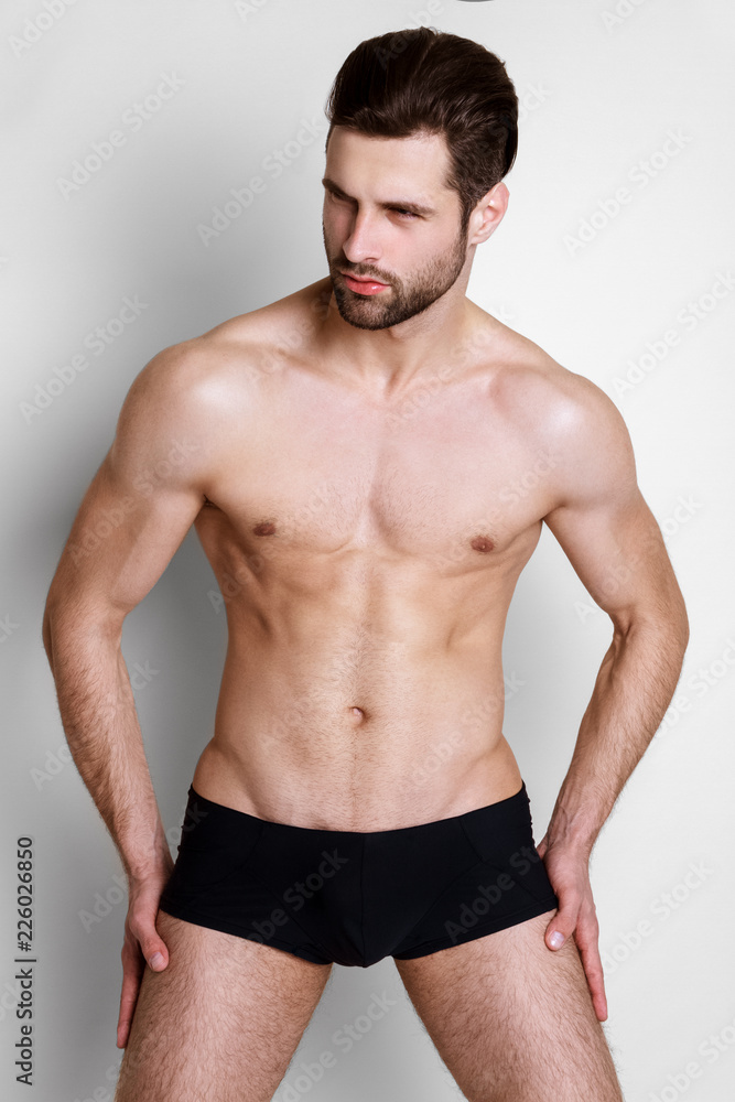 Handsome muscled strong face stripped male model in black underwear on white isolated font background