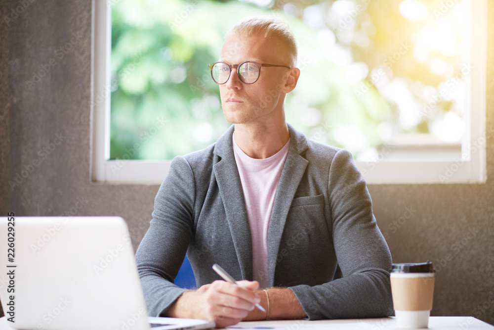 Fotografi Serious young manager in eyeglasses sitting at his workplace and working on lapt
