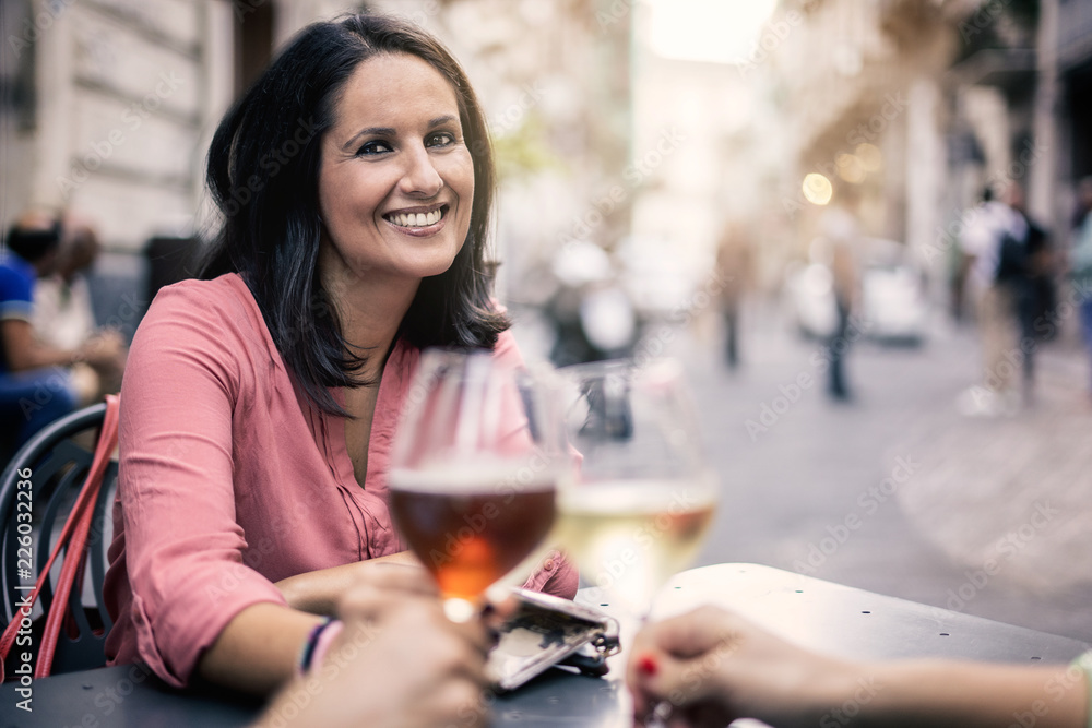 Adult woman having a celebrative toasting with a group of friend in a outdoor bar. Mid aged adult frienship and fun concept, mid season clothes.
