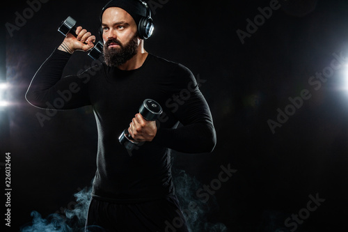 Muscular young fitness sports man, athlete workout with dumbbell and headphones in gym
