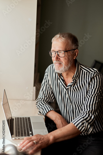 Senior man at home in front of laptop computer working. Freelancer, on line worker photo