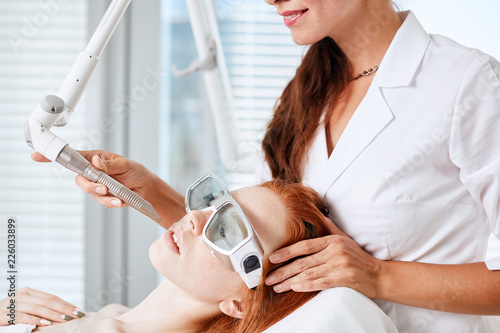 Red-haired female patient receiving fractional resurfacing, a laser treatment suitable for those wanting a global anti-age treatment. Modern cosmetological trends and technologies.
