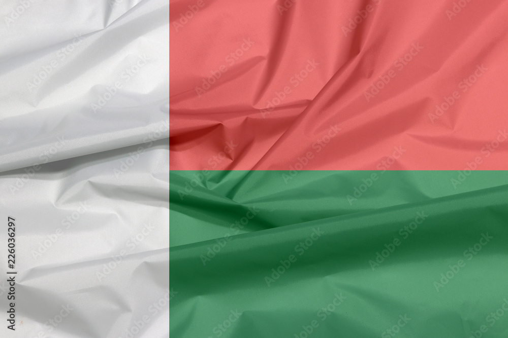 Obraz premium Fabric flag of Madagascar. Crease of Madagascar flag background, Two horizontal bands of red and green with a white vertical band on the hoist side.