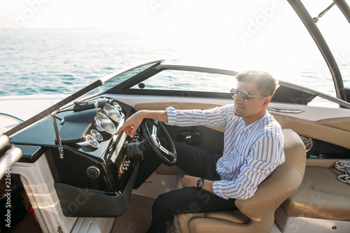 Cheerful professional sales manager sells luxury motor boats and yachts, holding the steering wheel in hands and demonstrating perfect boat s features photo