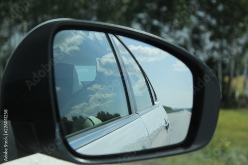 Reflection of the road, sky and clouds in the car rearview mirror