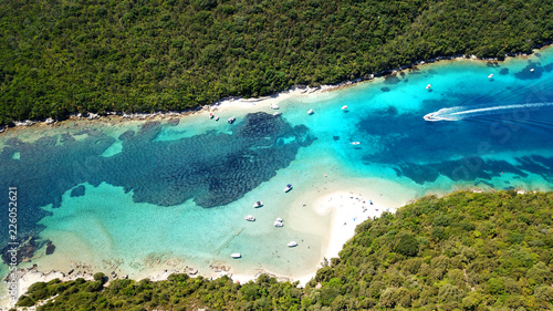 Aerial drone bird's eye view photo of popular and iconic turquoise beach of Bella Vraka in island of Mourtemeno with sunbeds and canoes forming a blue lagoon, Sivota bay, Epirus, Greece