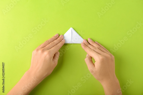 Woman making origami boat on color background