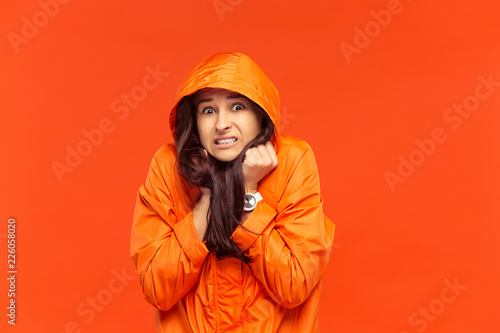 The young girl posing at studio in autumn jacket isolated on red. Human negative emotions. Concept of the cold weather. Female fashion concepts