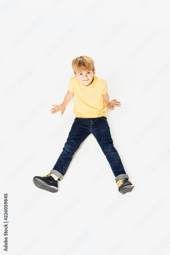 high angle view of adorable happy little boy sitting and smiling at camera isolated on white