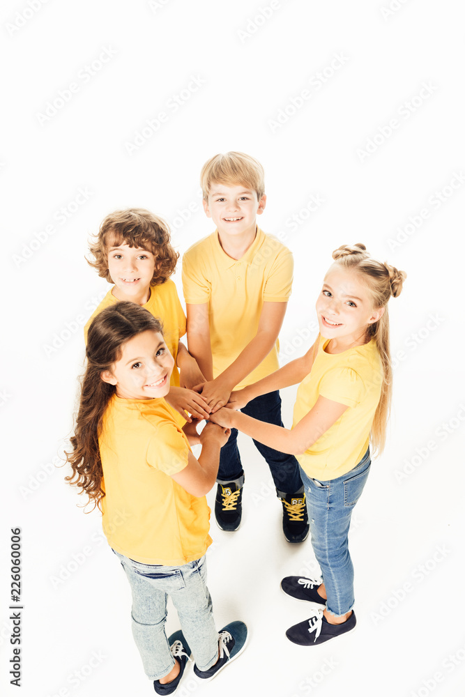 high angle view of adorable happy children stacking hands and smiling at camera isolated on white high angle view of adorable happy children stacking hands and smiling at camera isolated on white