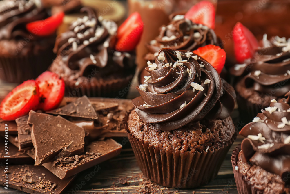 Tasty cupcakes with strawberry and pieces of chocolate bar on wooden table Tasty cupcakes with strawberry and pieces of chocolate bar on wooden table