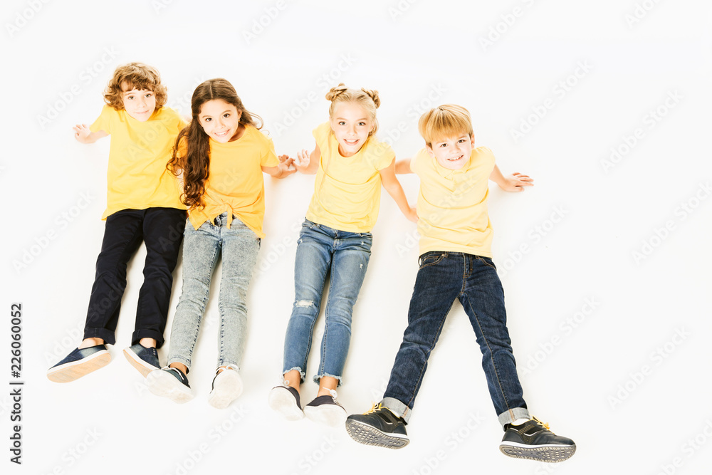 Obraz premium high angle view of adorable happy kids in yellow t-shirts sitting together and smiling at camera isolated on white