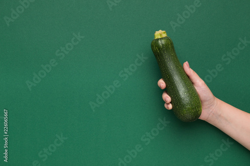Fresh zucchini in female hand on green background