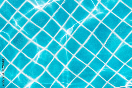 Blue tile on swimming pool bottom under clear water with sun light reflection. Travel  vacation concept. Text space.