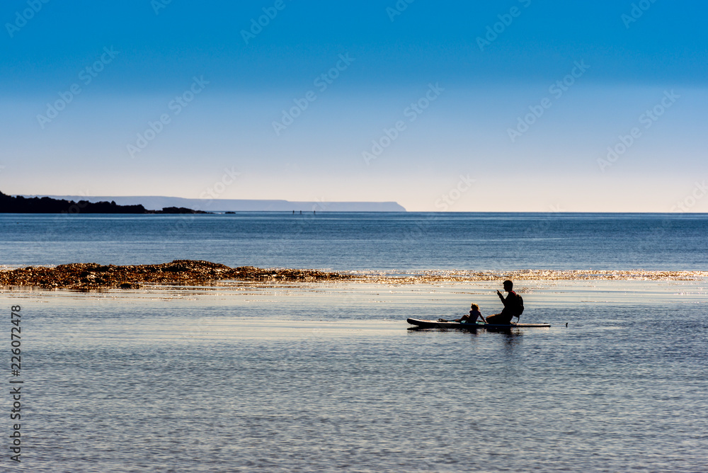 Silhouetted paddle boarder on a calm sea under clear sky