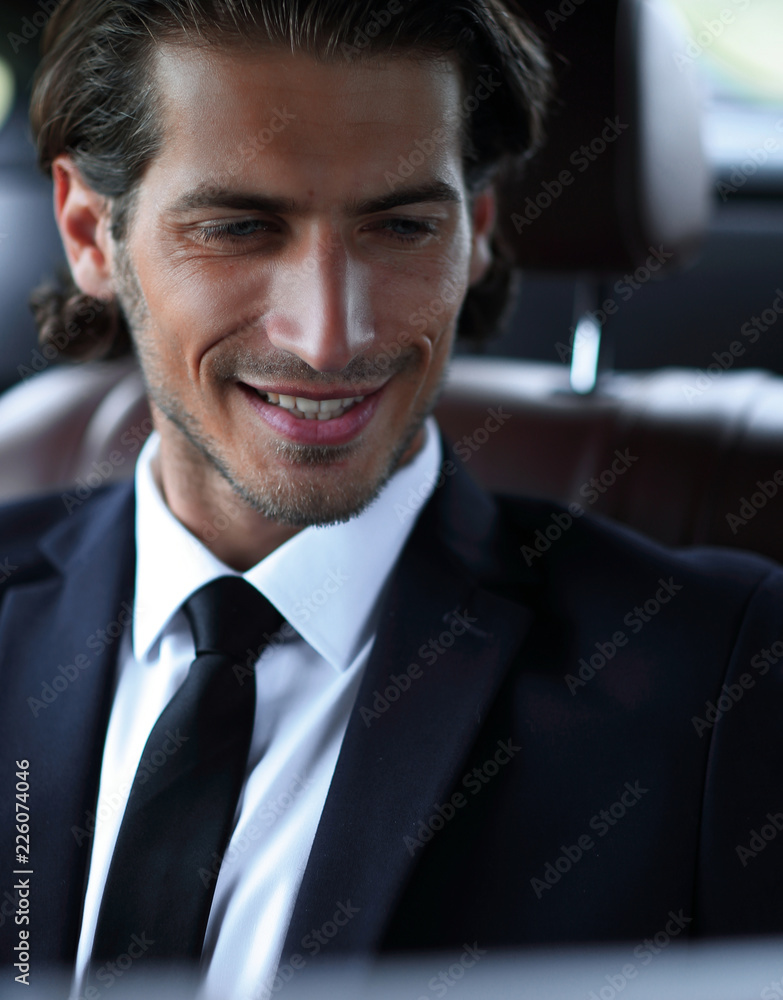 man sitting in the back-seat of a car, using his laptop
