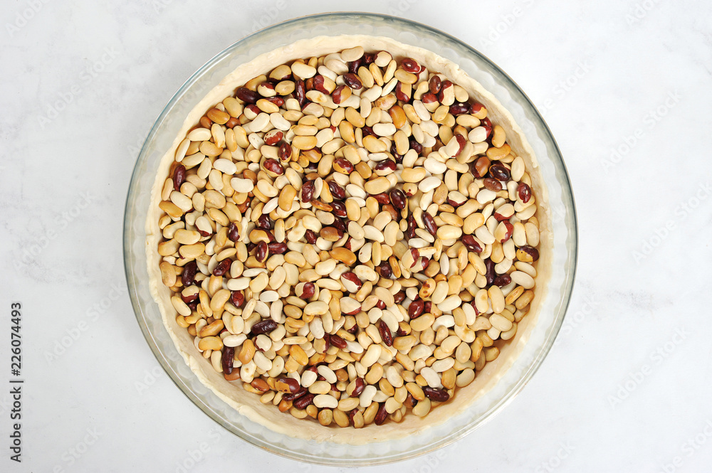 Dough in the form before baking. Put the beans on the dough to maintain the desired shape. Light background. Close-up. View from above. Dough in the form before baking. Put the beans on the dough to maintain the desired shape. Light background. Close-up. View from above.