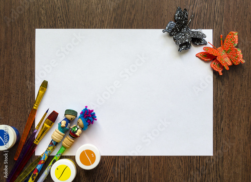 Empty white sheet of paper for your text. There are colored pencils, pens, paints around it. Mockup