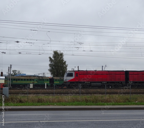 Pair of Two Red And Green Locomotives Trains On The Railroad Railway Behind Asphalt City Road And Grass