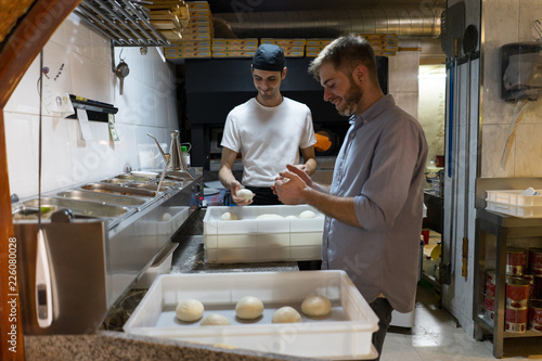 Two men with raw dough in boxes in kitchen of a pizzeria photo