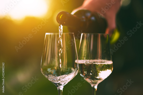 Pouring white wine into glasses at sunset
