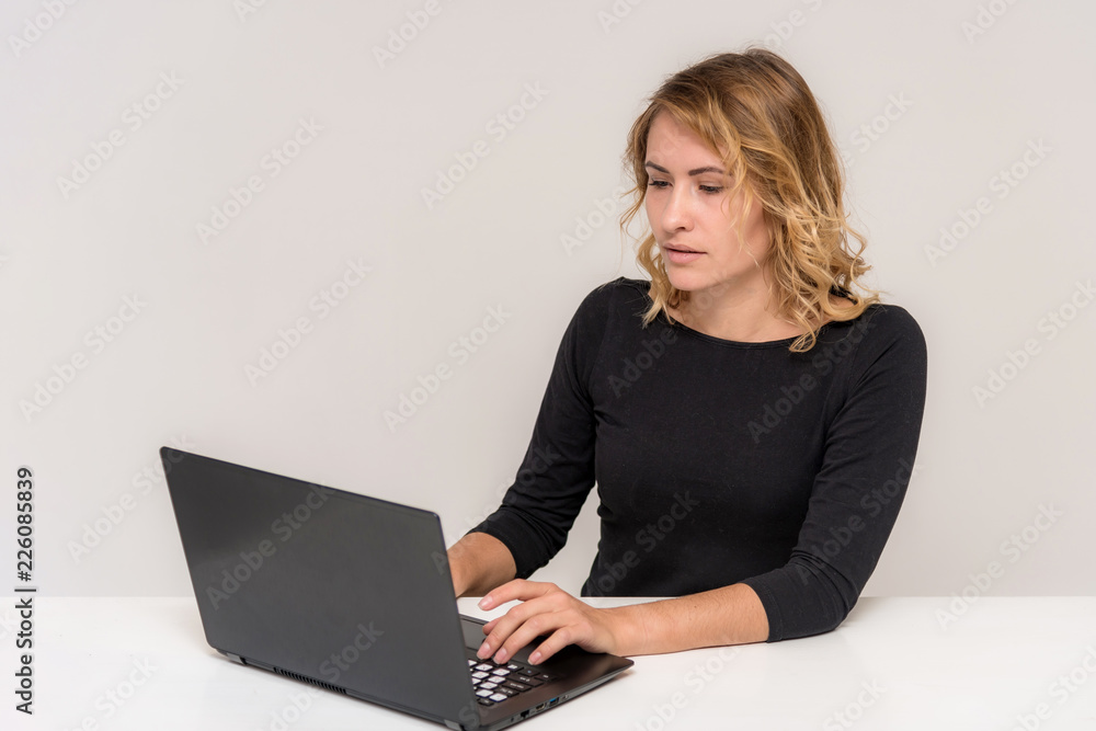 Portrait of a beautiful blonde girl on a white background at the table with a laptop. Portrait of a beautiful blonde girl on a white background at the table with a laptop.