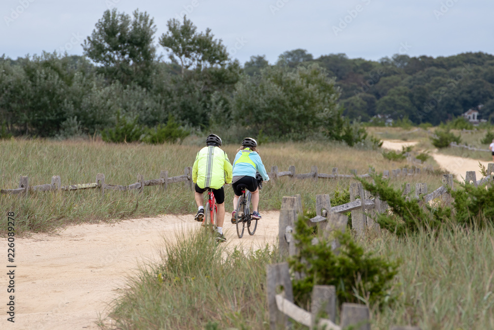 mature couple biking on a path in a park with trees and grass.