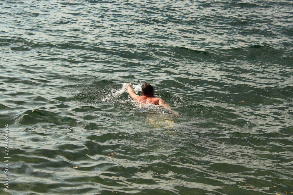A young man is swimming in the water. Swimmer swims over the lake.