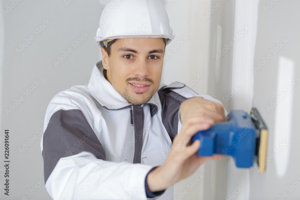 young handsome worker sanding wall at construction site