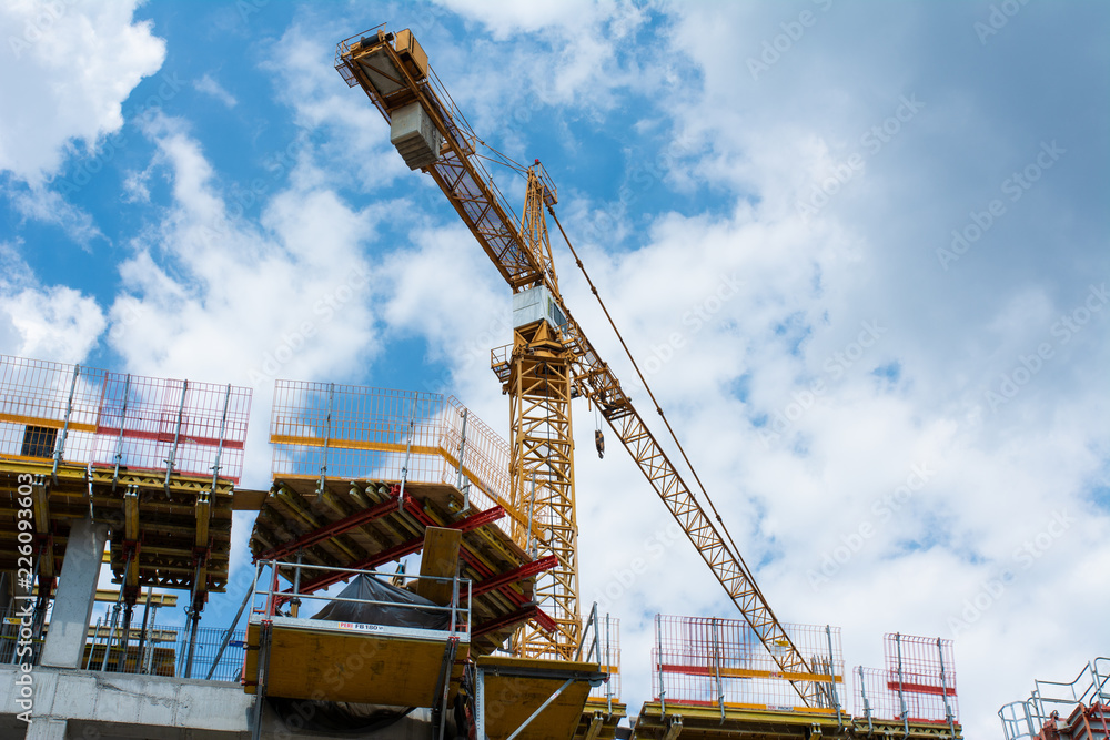 Construction of an apartment building in the center of a large city with the help of a construction crane. Photo taken from below on a background of blue sky. Construction of an apartment building in the center of a large city with the help of a construction crane. Photo taken from below on a background of blue sky.
