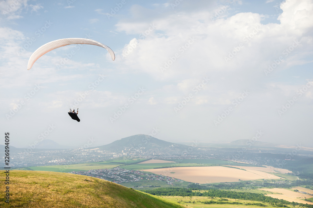 A white-orange paraglider flies over the mountainous terrain A white-orange paraglider flies over the mountainous terrain