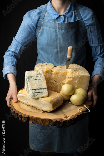 Rustic gourmet italian cheese on wooden board in hands of cheese maker on black background