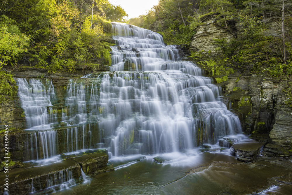 Fototapeta premium Beautiful sunrise over Hector Falls at Watkins Glen, upstate New York, featuring sun beaming trough the trees on the background