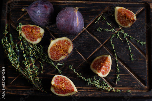 Ripe figs on a dark wooden board next to sprigs of thyme for tea