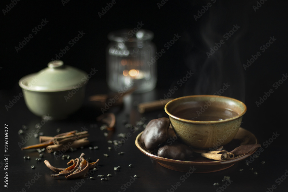 Cozy dark still life with cup of hot tea with gingerbread cookies, cinnamon and dried pears and candle in the background Cozy dark still life with cup of hot tea with gingerbread cookies, cinnamon and dried pears and candle in the background