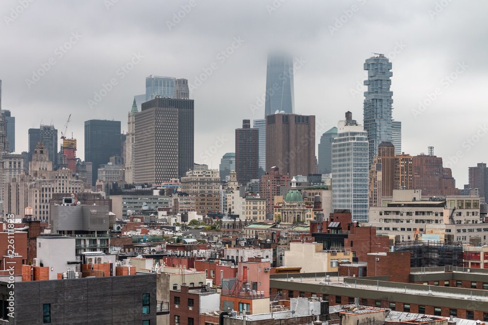 A cityscape of lower Manhattan looking from south of Houston toward the financial area of New York City. The clouds are low and obscuring some of the tallest buildings. 