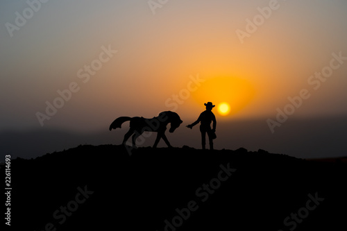 Cowboy concept. Silhouette of Cowboys at sunset time. A cowboy silhouette on a mountain with an yellow sky. © zef art