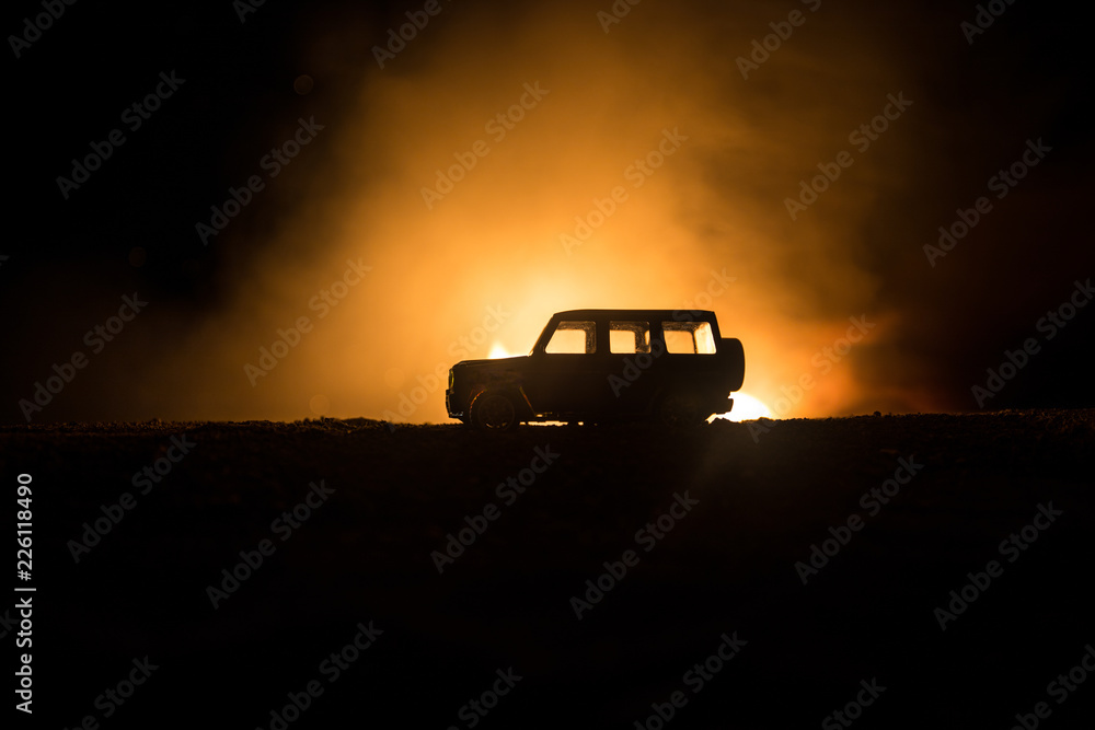 Off roader jeep silhouette on dark toned foggy sky background. Car with light at night. Off roader jeep silhouette on dark toned foggy sky background. Car with light at night.