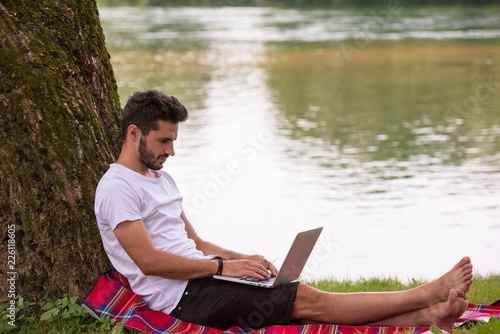 man using a laptop computer on the bank of the river